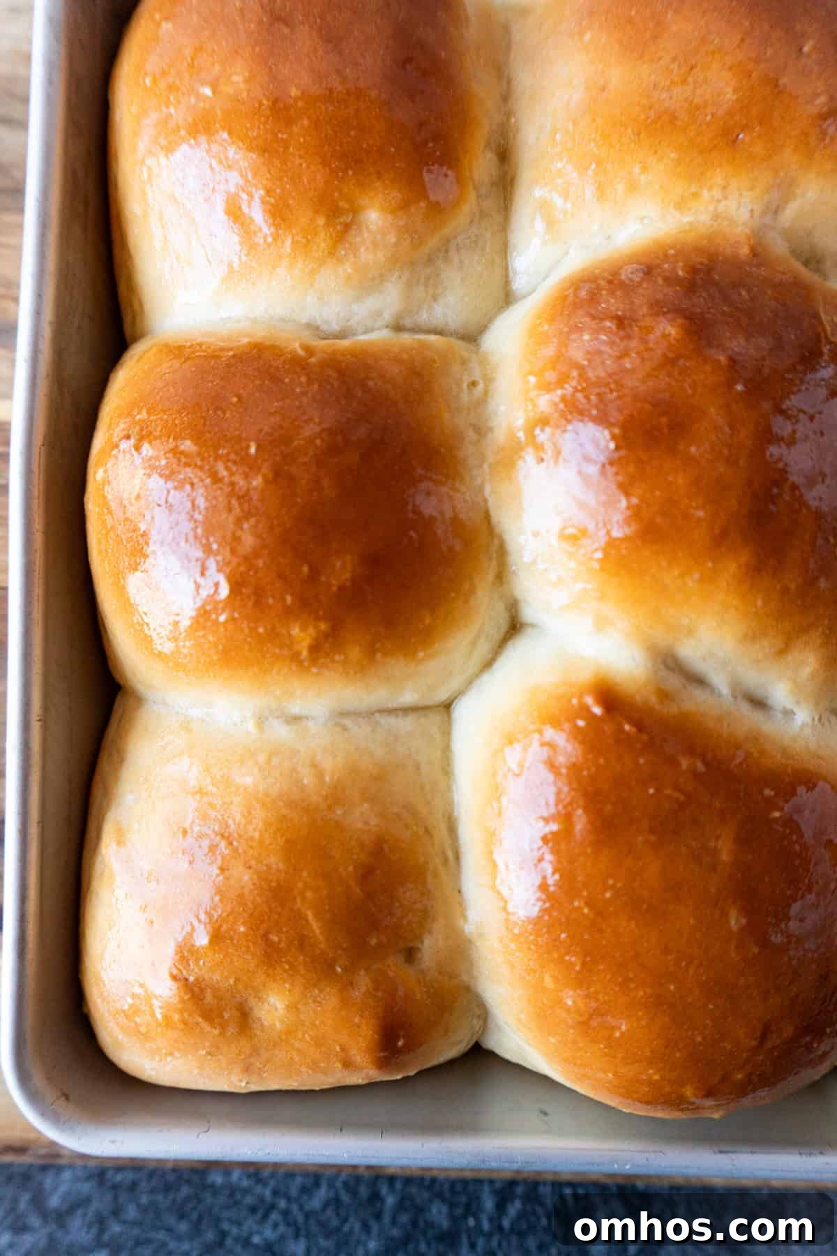 Fluffy Soft Dinner Rolls: Buttery Homemade Recipe 3 baked soft dinner rolls with golden tops and shiny melted butter still in baking dish.