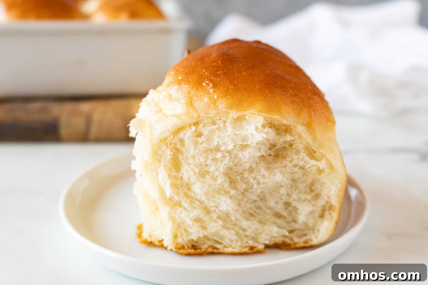 Fluffy Soft Dinner Rolls: Buttery Homemade Recipe 5 soft dinner roll on white plate with golden top.
