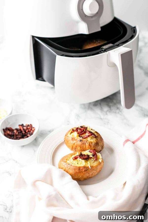 Air Fryer baked potatoes with melted cheese and bacon bits served on a white plate.