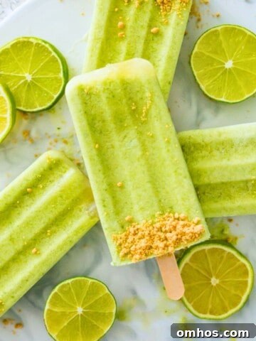 Four key lime pie popsicles stacked on top of each other with lime wedges around them.