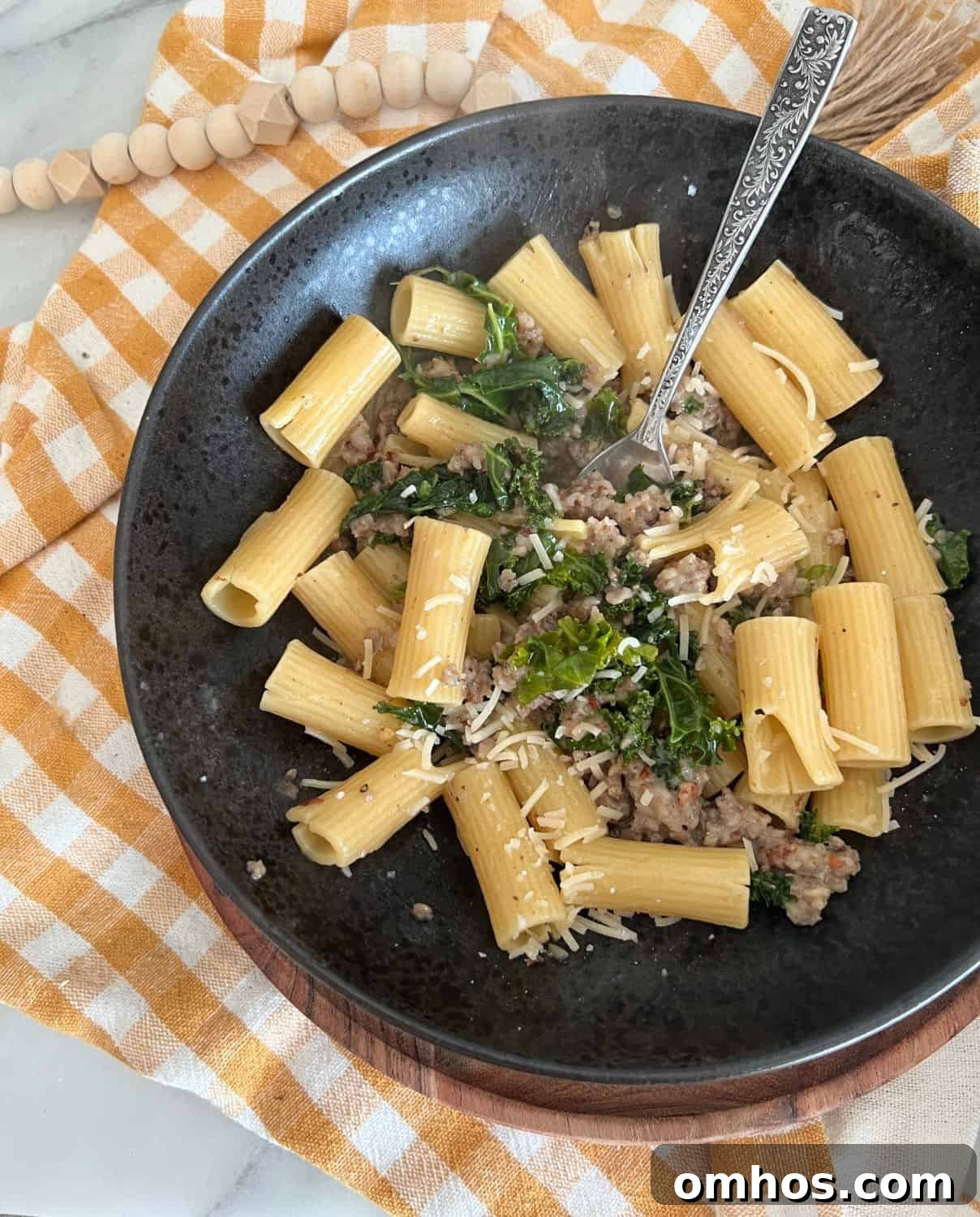 Finished rigatoni with sausage and kale in a black bowl with a fork.
