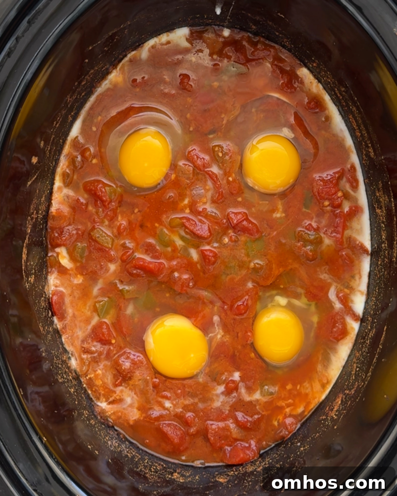 overhead shot of cooked slow cooker shakshuka in a black slow cooker with raw eggs added