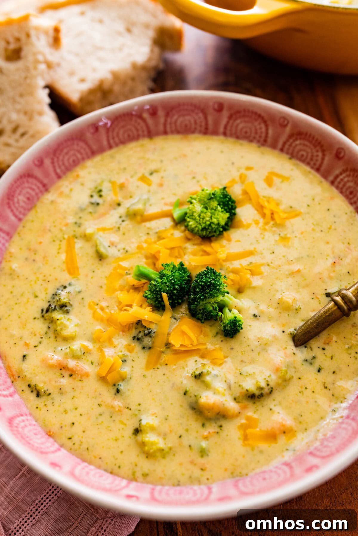 Broccoli cheddar soup recipe in a pink bowl with a spoon in it ready to serve. 