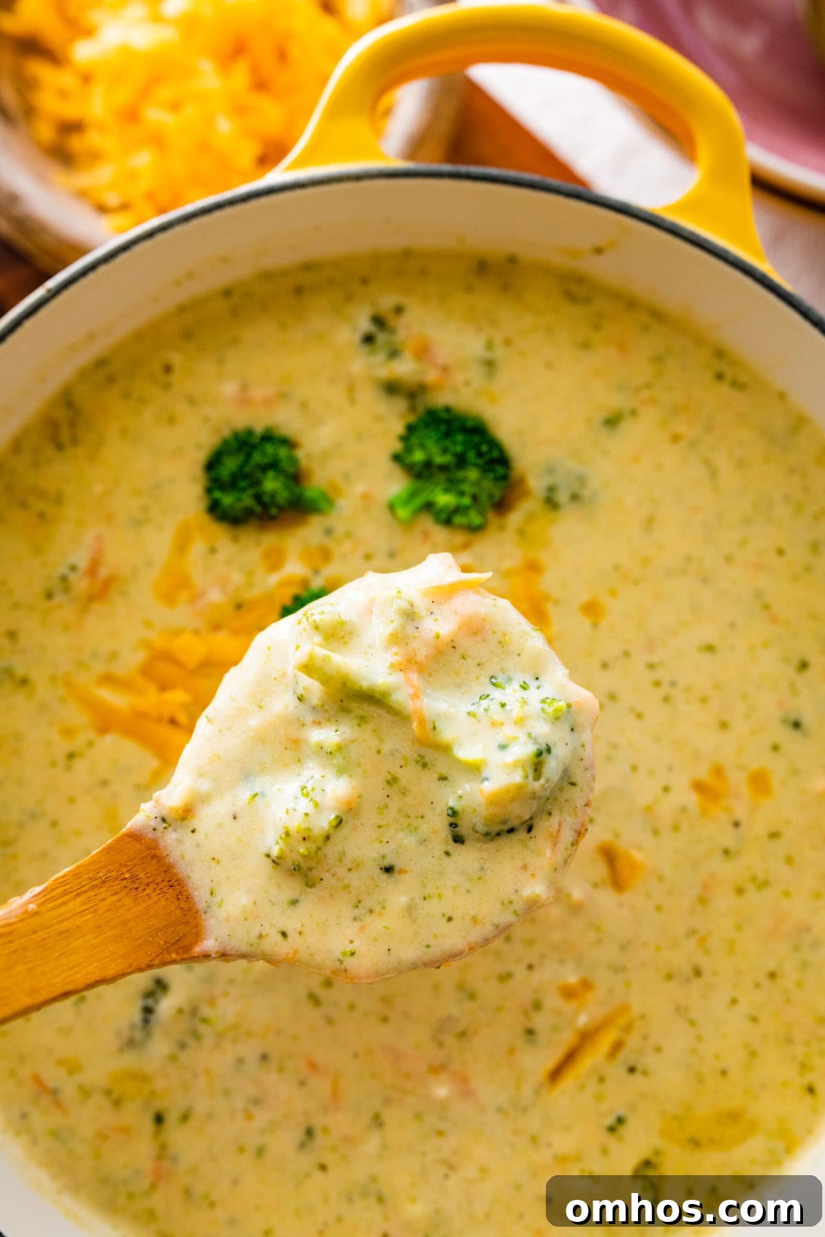 Copycat Panera Broccoli Cheddar Soup Recipe in a soup pot with a wooden ladle. Ladle holding up a serving of the soup ready to serve.