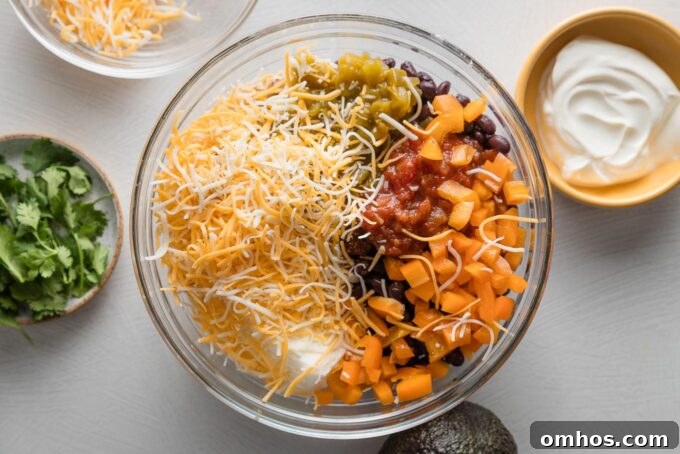 Crispy Baked Chicken and Black Bean Taquitos 5 Clear glass prep bowl filled with shredded chicken, cheese, veggies, black beans, and spices.