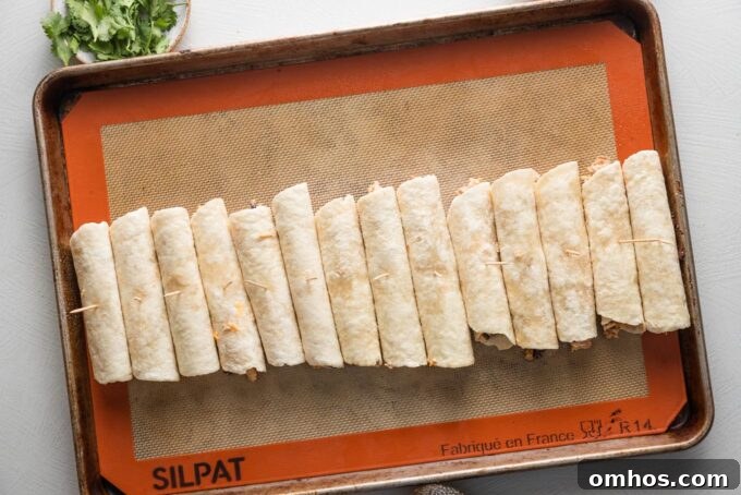 Crispy Baked Chicken and Black Bean Taquitos 7 Rolled taquitos arranged on a baking tray.