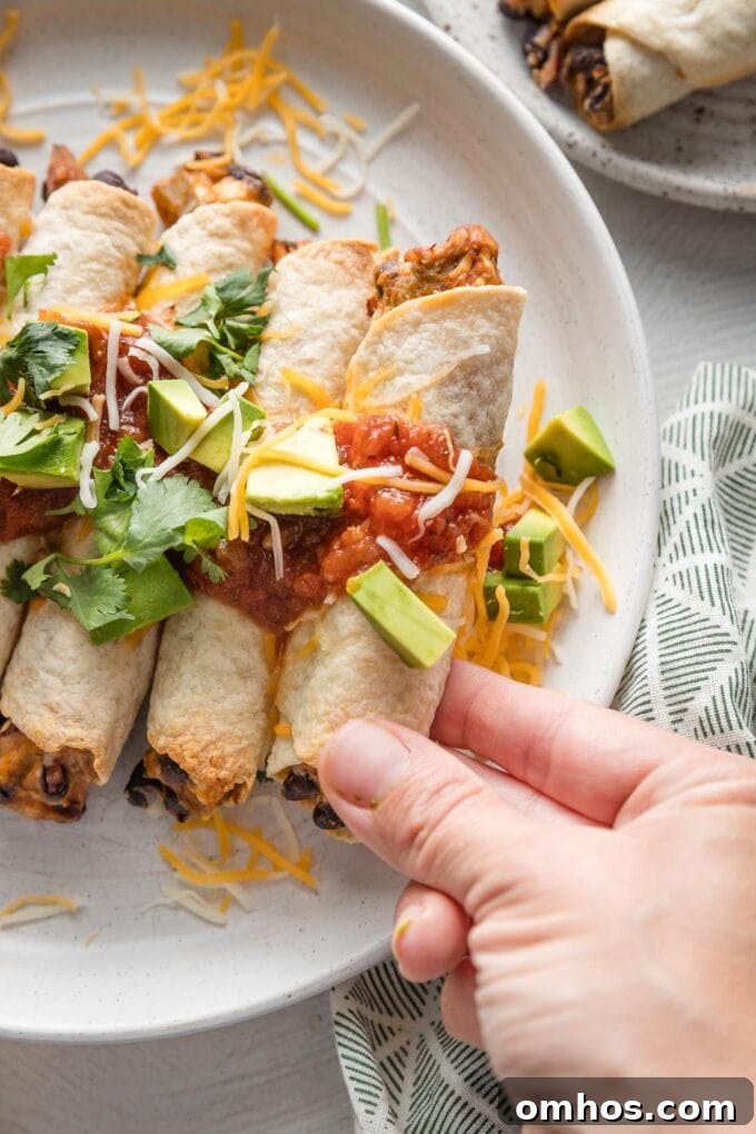 Crispy Baked Chicken and Black Bean Taquitos 8 Hand holding up a chicken black bean taquito straight out of the oven and placed on a serving plate.