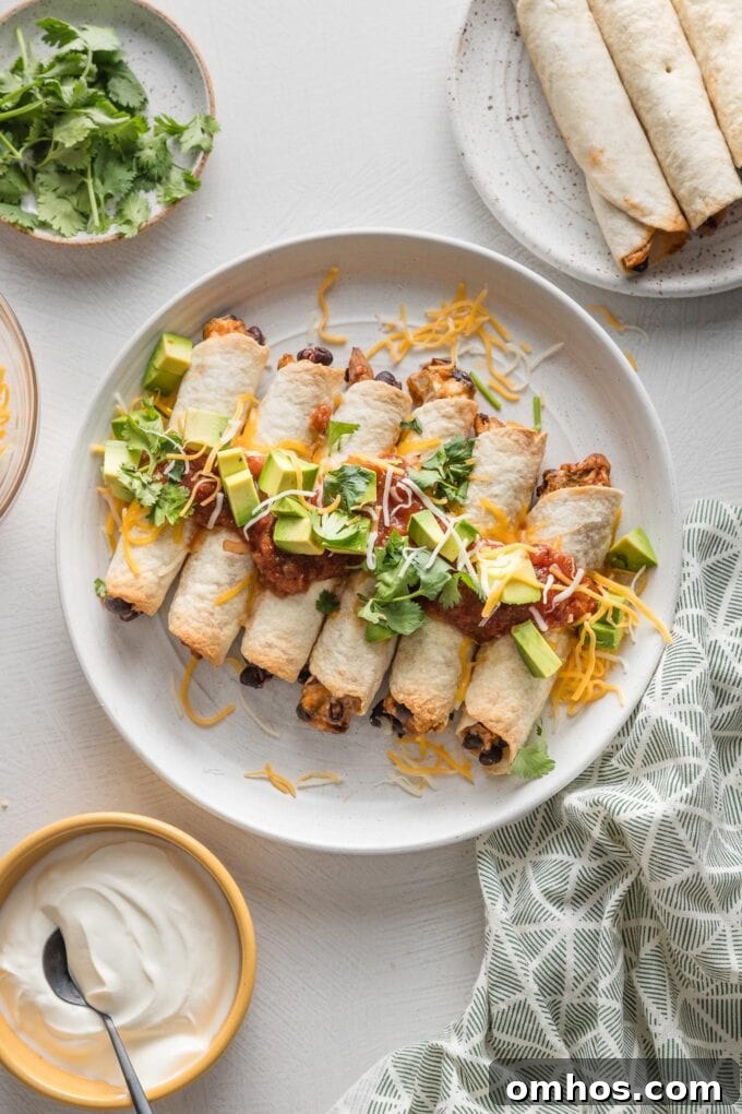 Crispy Baked Chicken and Black Bean Taquitos 9 Countertop set with a large plate of chicken black bean taquitos surrounded by fresh cilantro, sour cream, and extra garnishes.