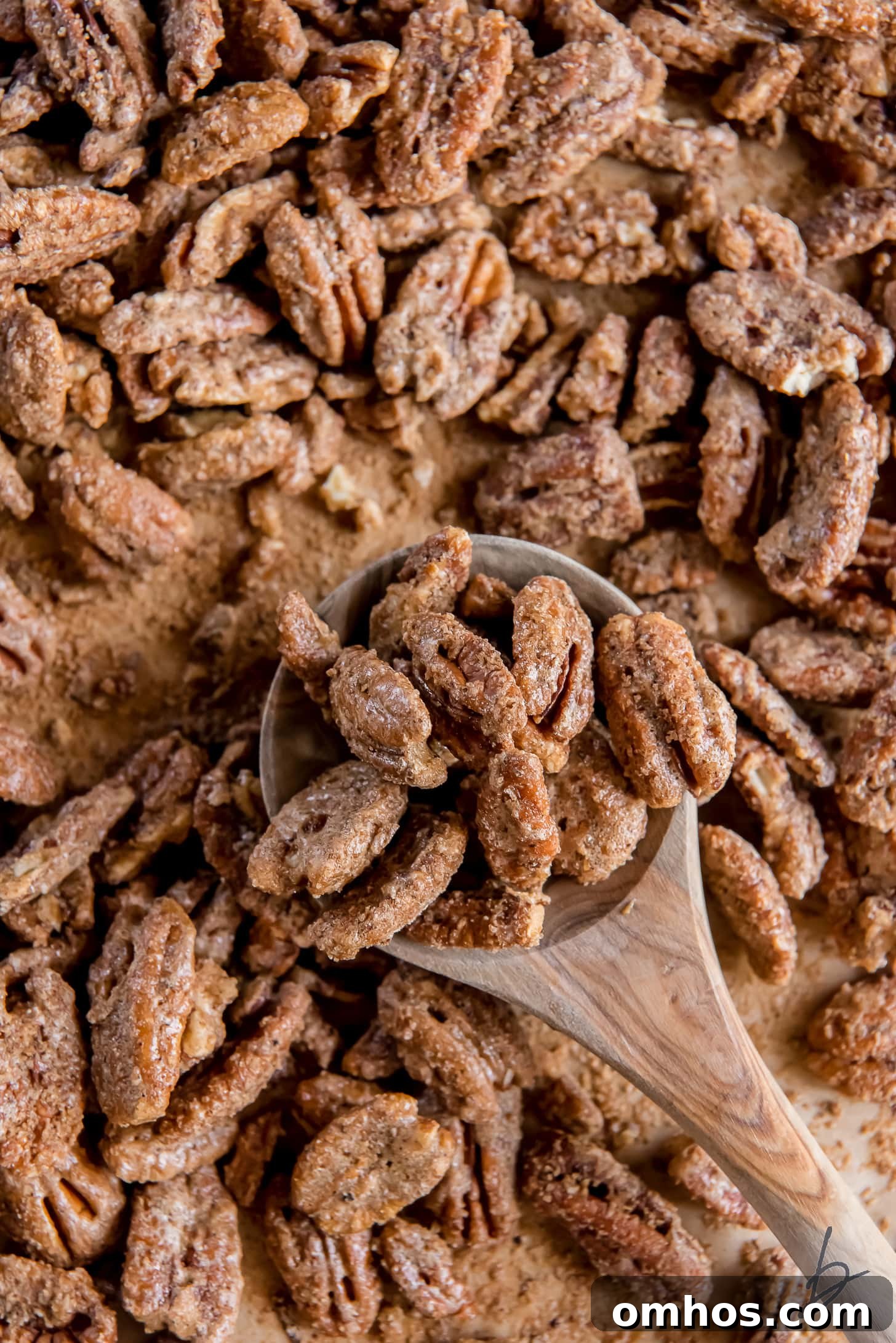 wooden spoon holding spiced pecans on baking sheet with more pecans.