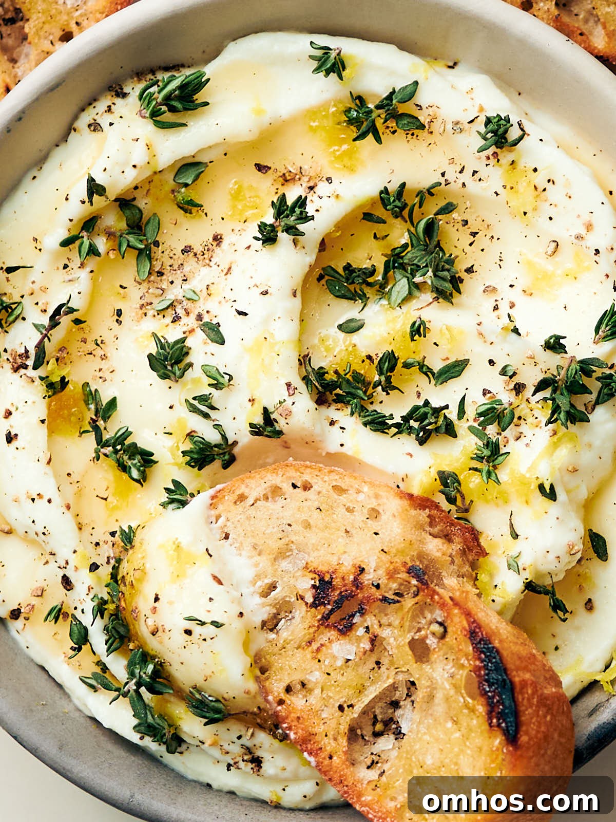 Creamy Whipped Ricotta Dip with Honey 11 A piece of bread being dipped into creamy whipped ricotta dip in a bowl.