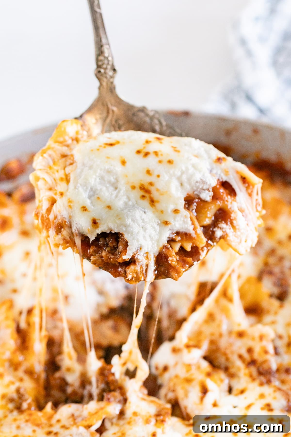 A spoon pulling up a scoop of skillet lasagna with melted cheese stretching behind it.