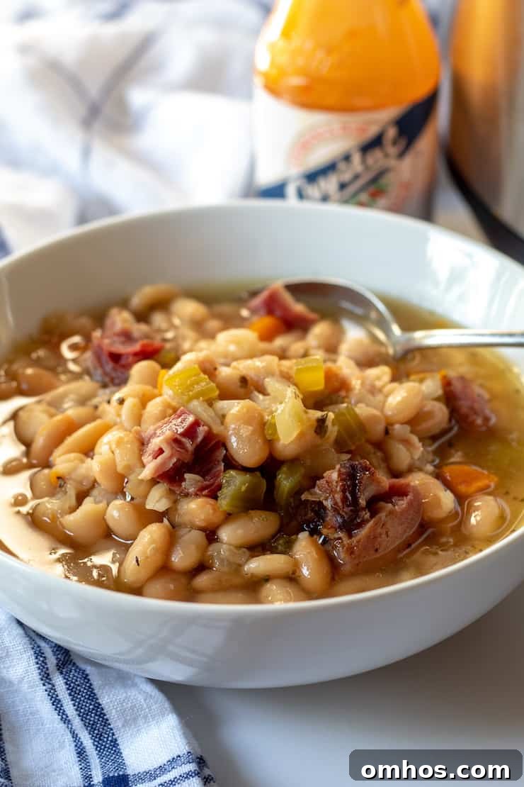 Hearty Instant Pot Ham and White Bean Soup 2 Ham and bean soup in bowl with spoon and hot sauce in background.
