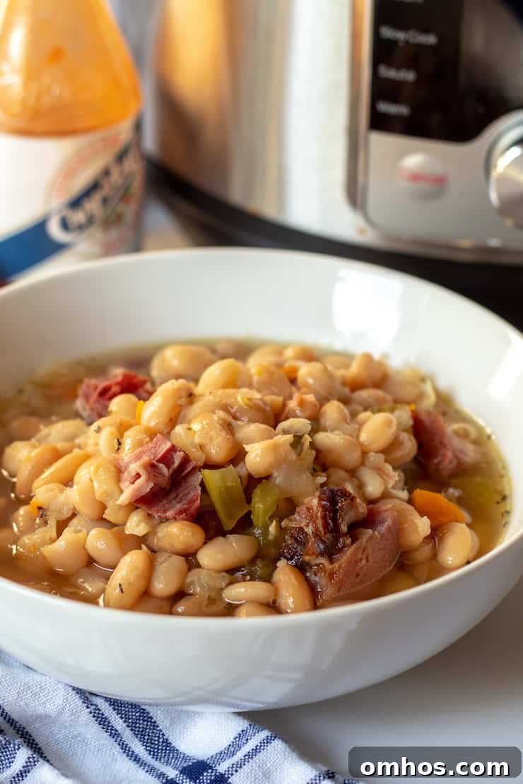 Hearty Instant Pot Ham and White Bean Soup 3 Soup in bowl with Instant Pot and hot sauce in background.