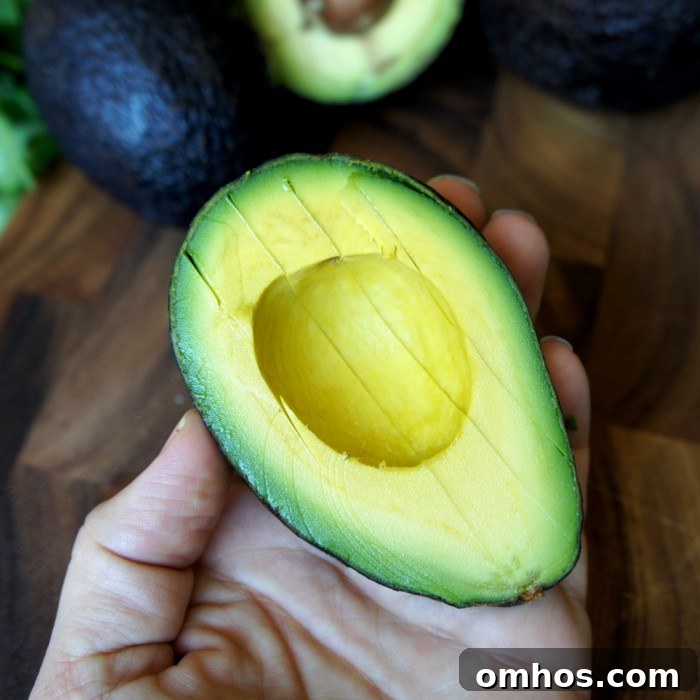 Half an avocado with slices made into it resting in a hand.