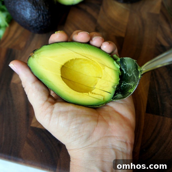A hand holding half an avocado with a spoon removing the avocado from the skin