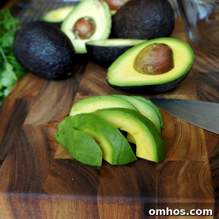 A sliced avocado on a cutting board in front of many halves of an avocado