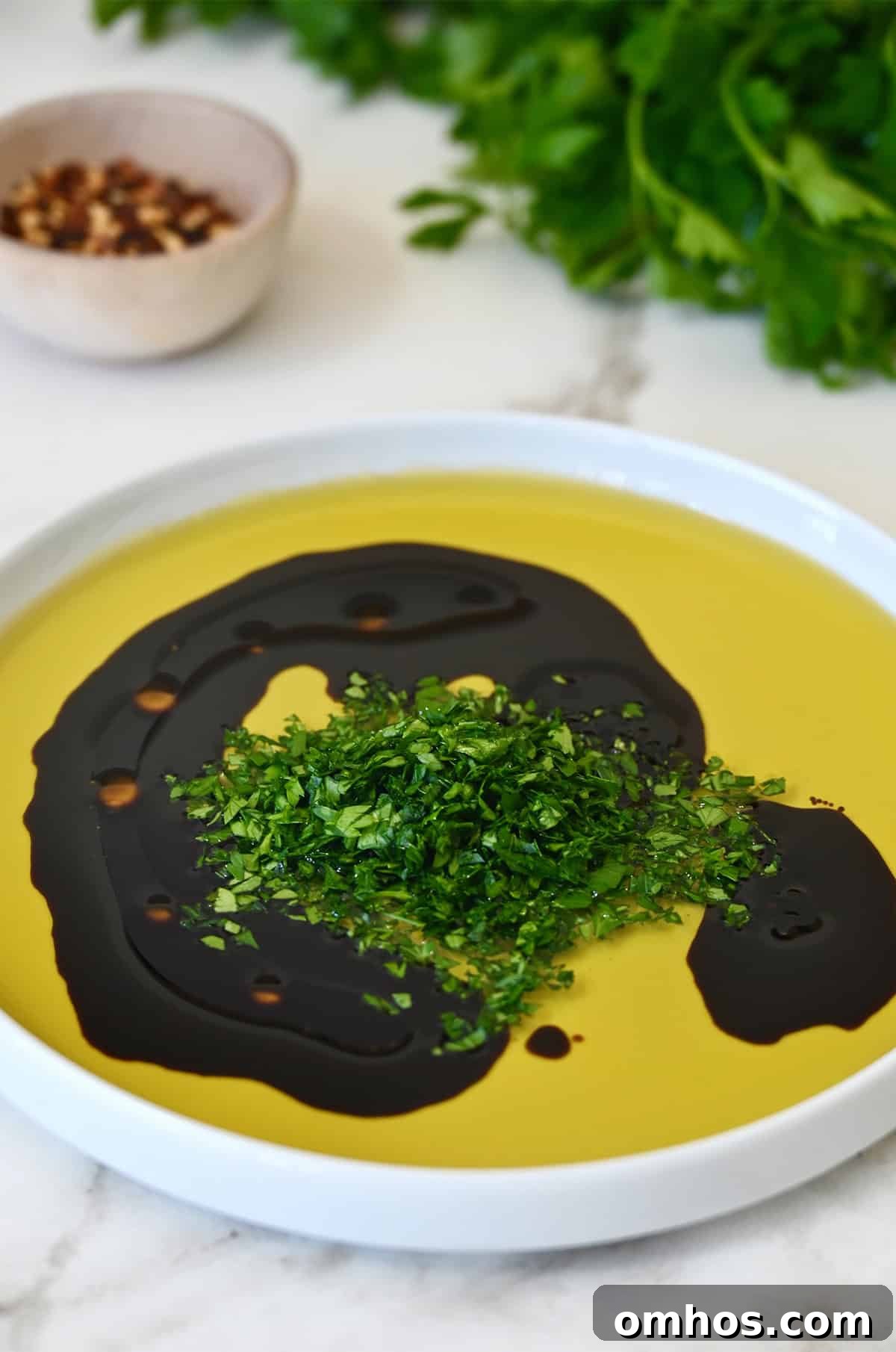 Finely chopped fresh parsley in a shallow plate with olive oil and balsamic vinegar.