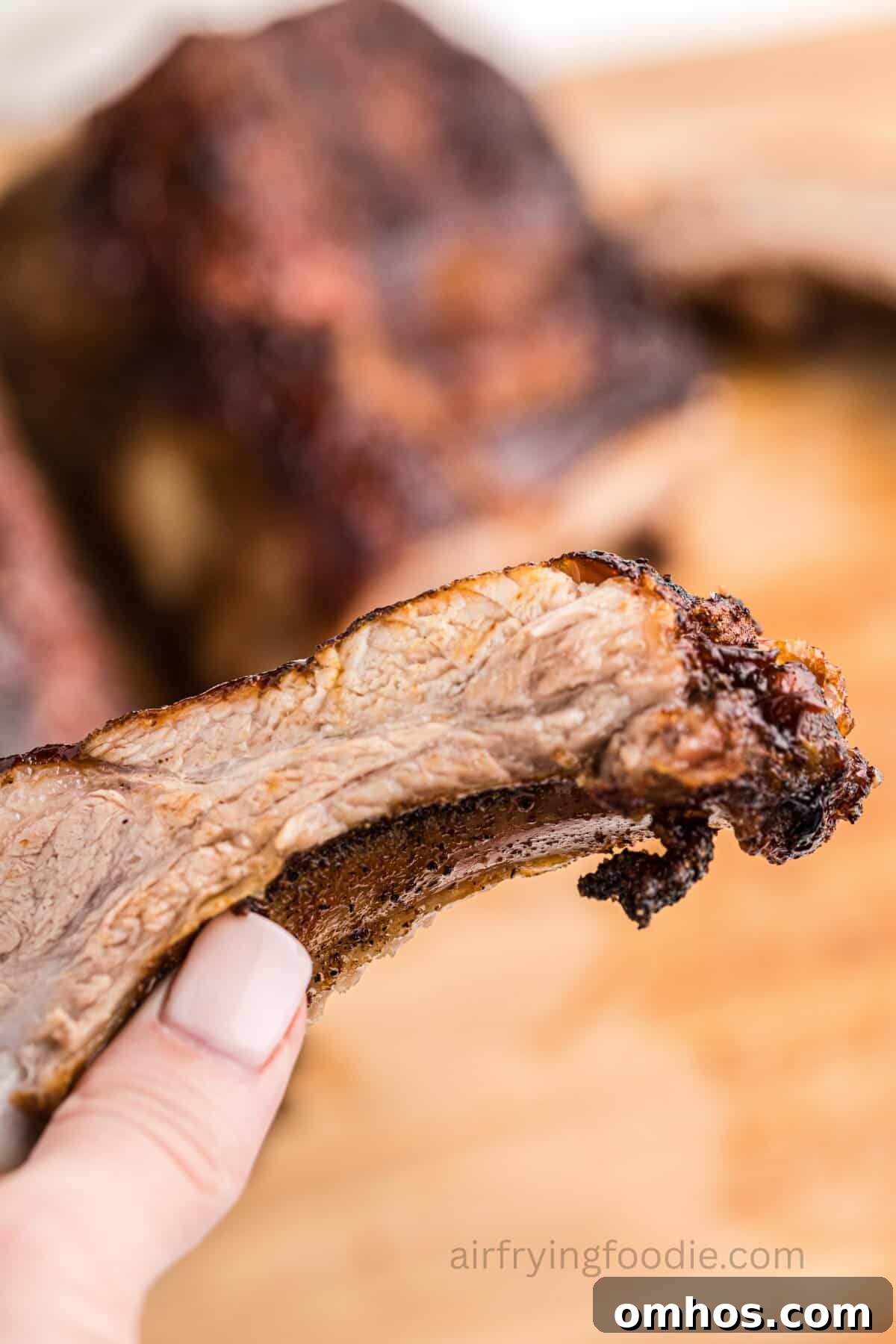 Crispy Air Fryer BBQ Ribs Recipe with Sticky Glaze 7 A hand holding up an air-fried BBQ rib.