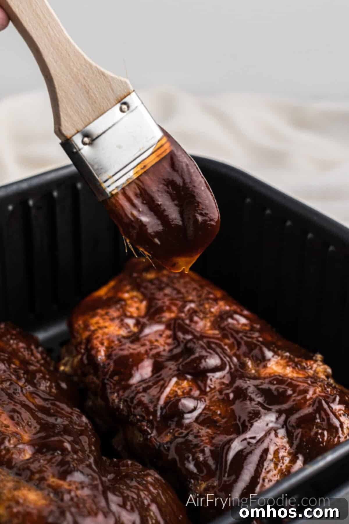 Crispy Air Fryer BBQ Ribs Recipe with Sticky Glaze 8 BBQ ribs in the air fryer basket with a brush adding some more sauce.