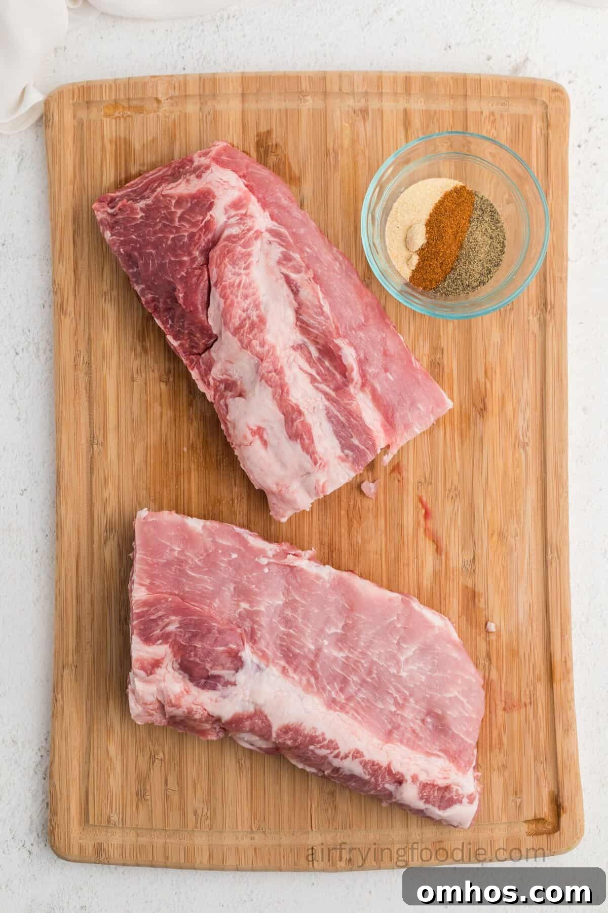 Crispy Air Fryer BBQ Ribs Recipe with Sticky Glaze 5 Ribs on a cutting board with seasonings in a small bowl.