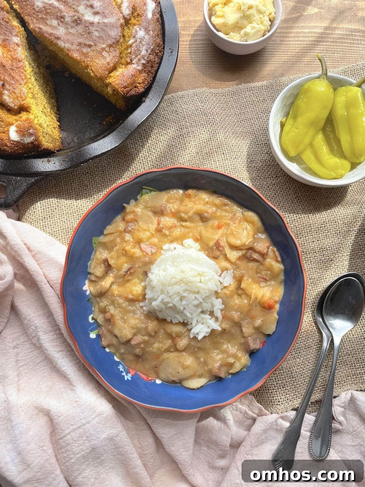 A blue bowl of butterbeans with a scoop of rice on top, pepperoncini peppers, and honey butter and sweet potato cornbread on the side.