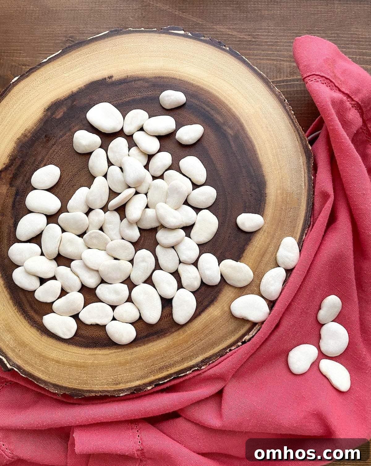 A wood platter with dry large lima beans spread across it.