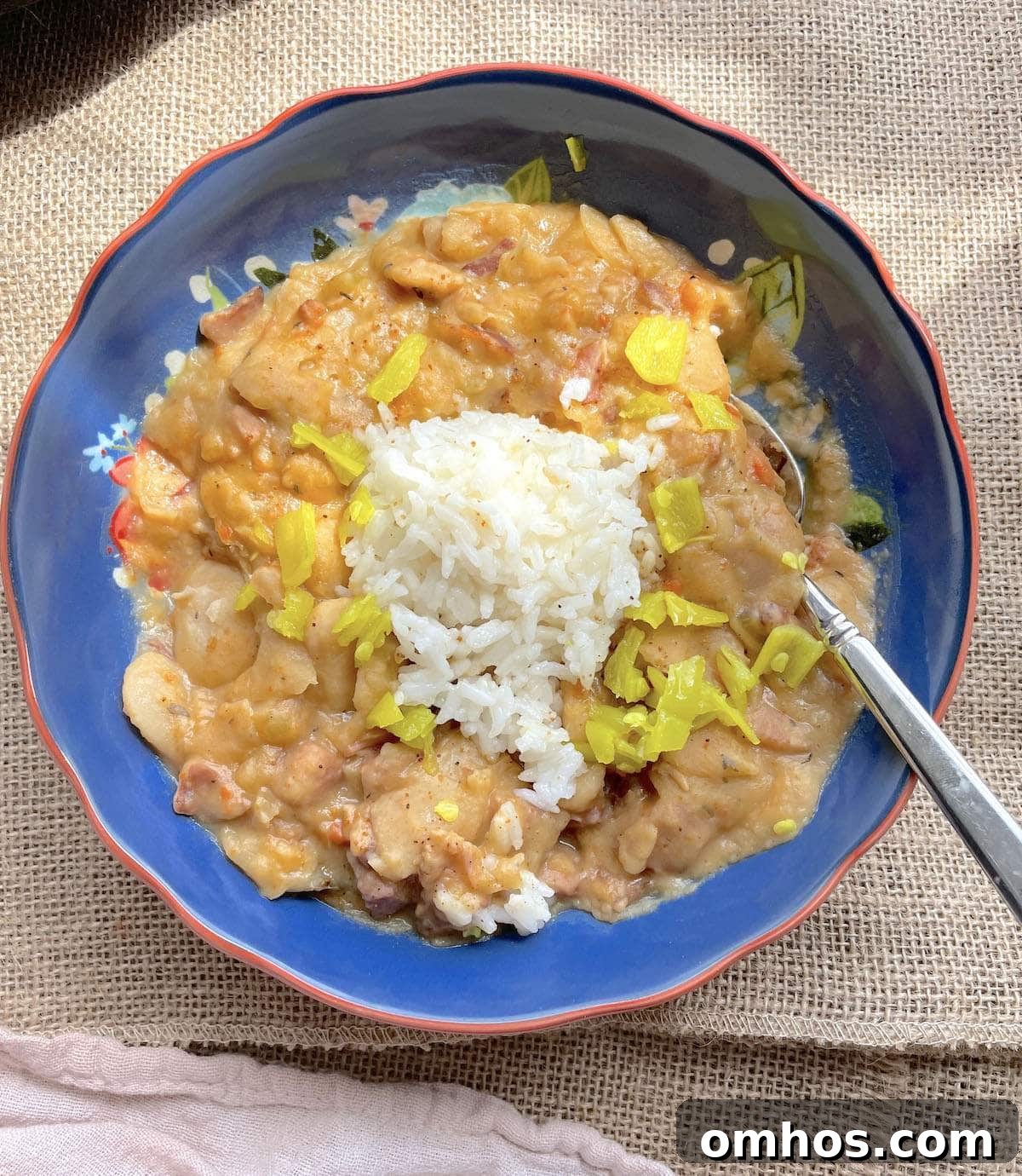 A blue bowl of creamy Southern style lima beans with a scoop of rice and pepperoncini peppers on top.