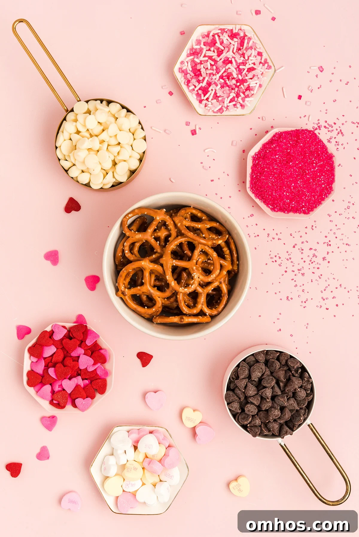 Valentine Pretzel Snack Bites Recipe 12 Bowl of Valentine Pretzel Snack Bites with chocolate chips, heart candies, and pink sprinkles on a pink background—a perfect Valentine’s Day treat.