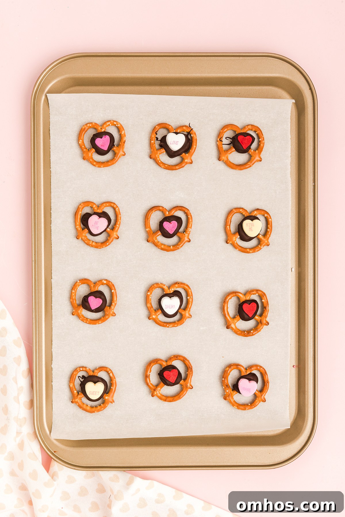 Valentine Pretzel Snack Bites Recipe 17 A baking tray with 12 heart-shaped Valentine Pretzel Snack Bites, each topped with chocolate and colorful candy hearts—perfect as a sweet Valentine’s Day treat.