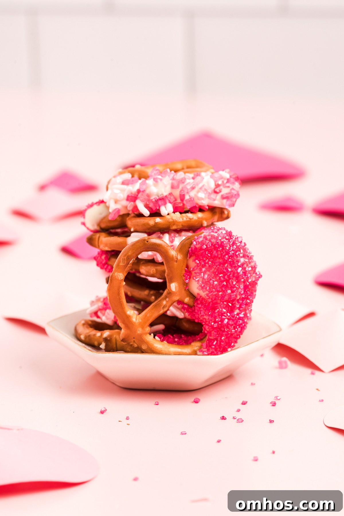 Valentine Pretzel Snack Bites Recipe 4 A stack of Valentine pretzels decorated with pink, white, and red sprinkles sits on a small white dish, making the perfect Valentine’s Day treat.