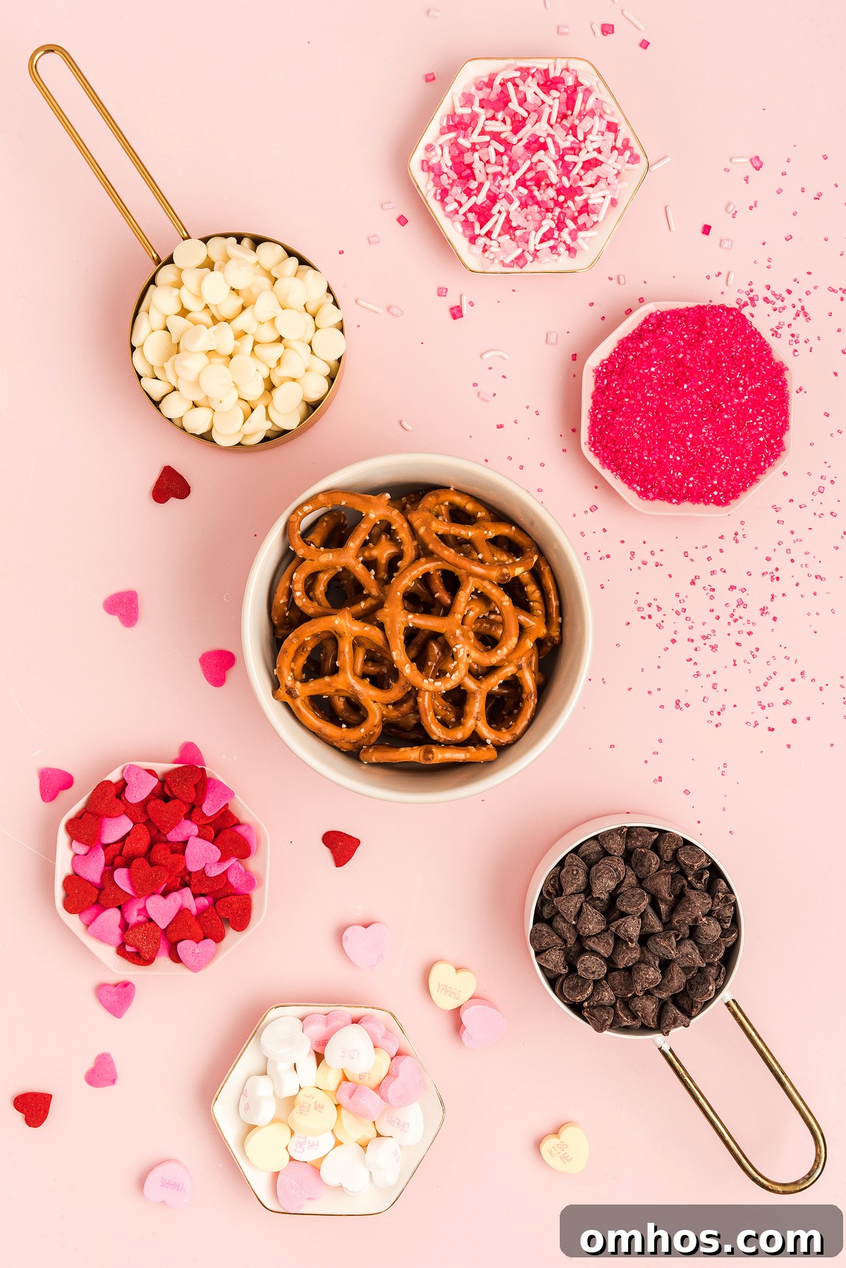 Valentine Pretzel Snack Bites Recipe 5 Bowl of Valentine Pretzel Snack Bites with chocolate chips, heart candies, and pink sprinkles on a pink background—a perfect Valentine’s Day treat.