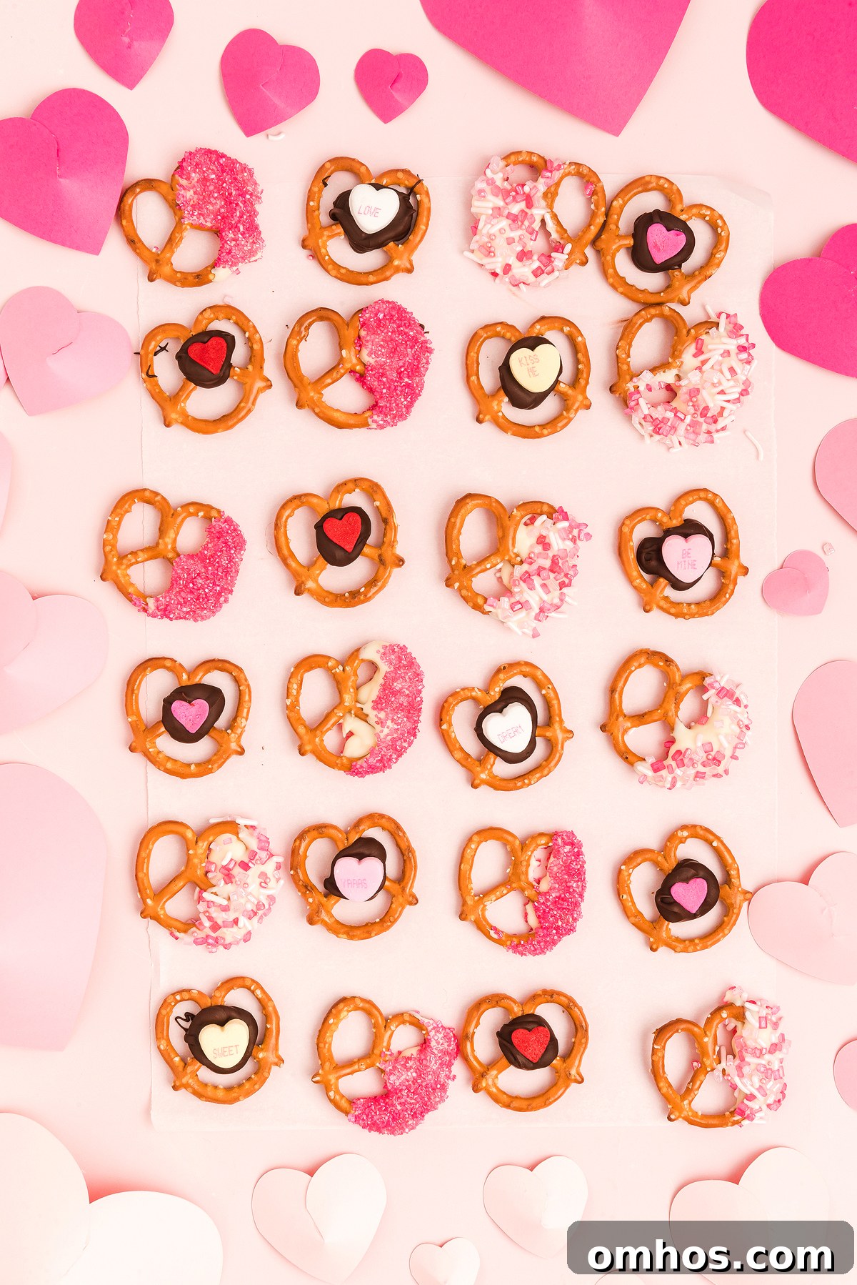 Valentine Pretzel Snack Bites Recipe 9 Heart-shaped Valentine pretzels with pink, red, and white decorations on a pink background with paper hearts make the perfect Valentine’s Day treat.