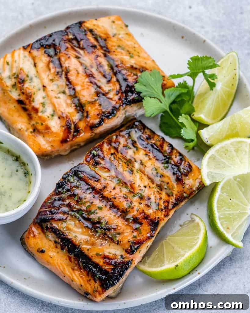 top view of 2 grilled salmon fillets on a white plate with lime slices to garnish