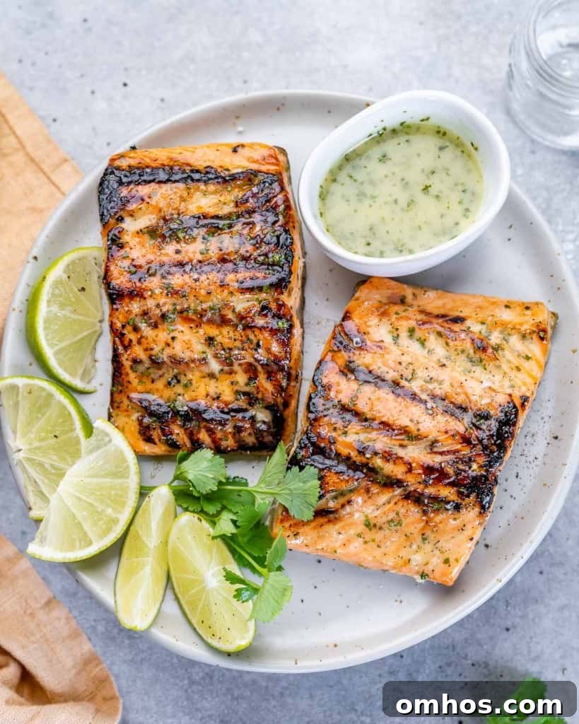 two grilled salmon filets on a white plate with lime garnishes and cilantro lime drizzle in a small bowl