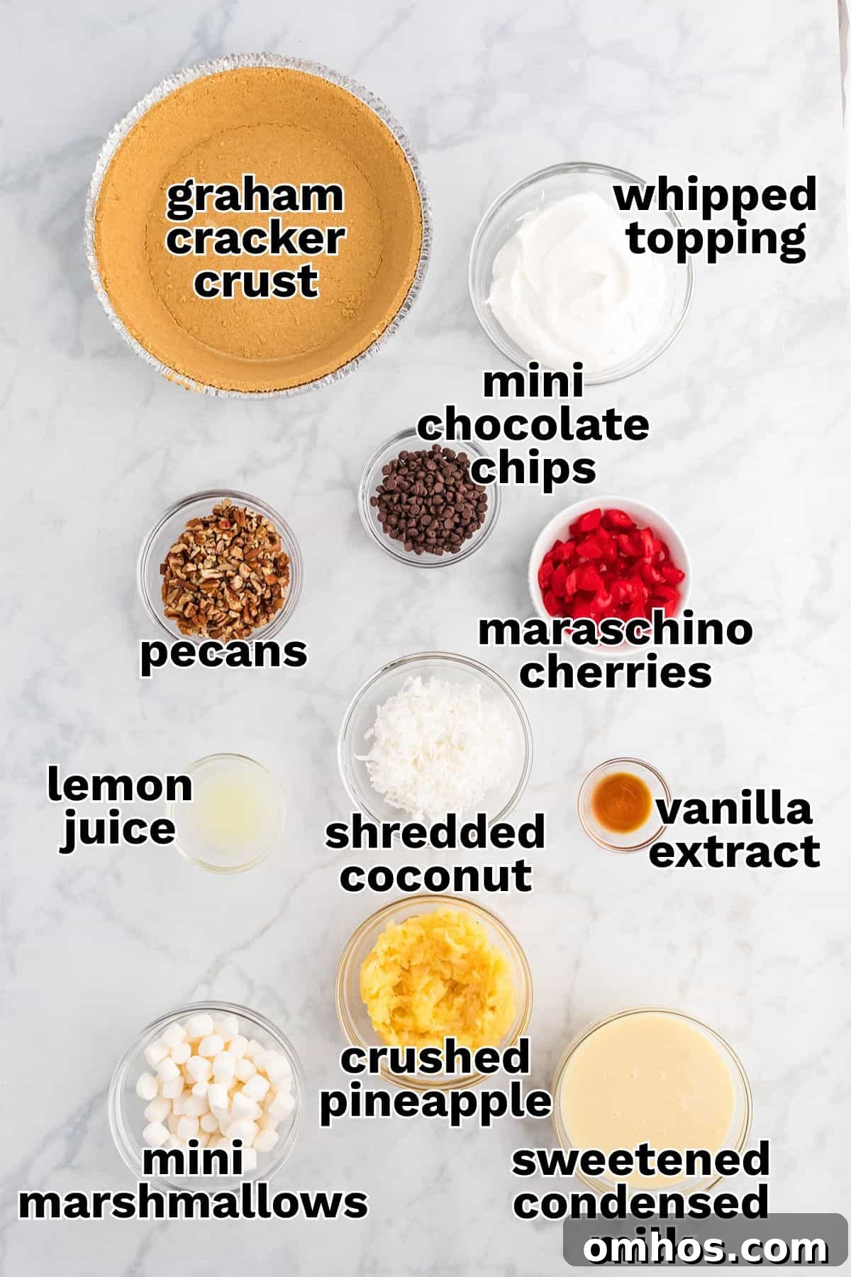 Ingredients for Million Dollar Pie dessert arranged on a marble surface, including graham cracker crust, whipped topping, mini chocolate chips, maraschino cherries, pecans, lemon juice, shredded coconut, crushed pineapple, mini marshmallows, vanilla extract, and sweetened condensed milk.