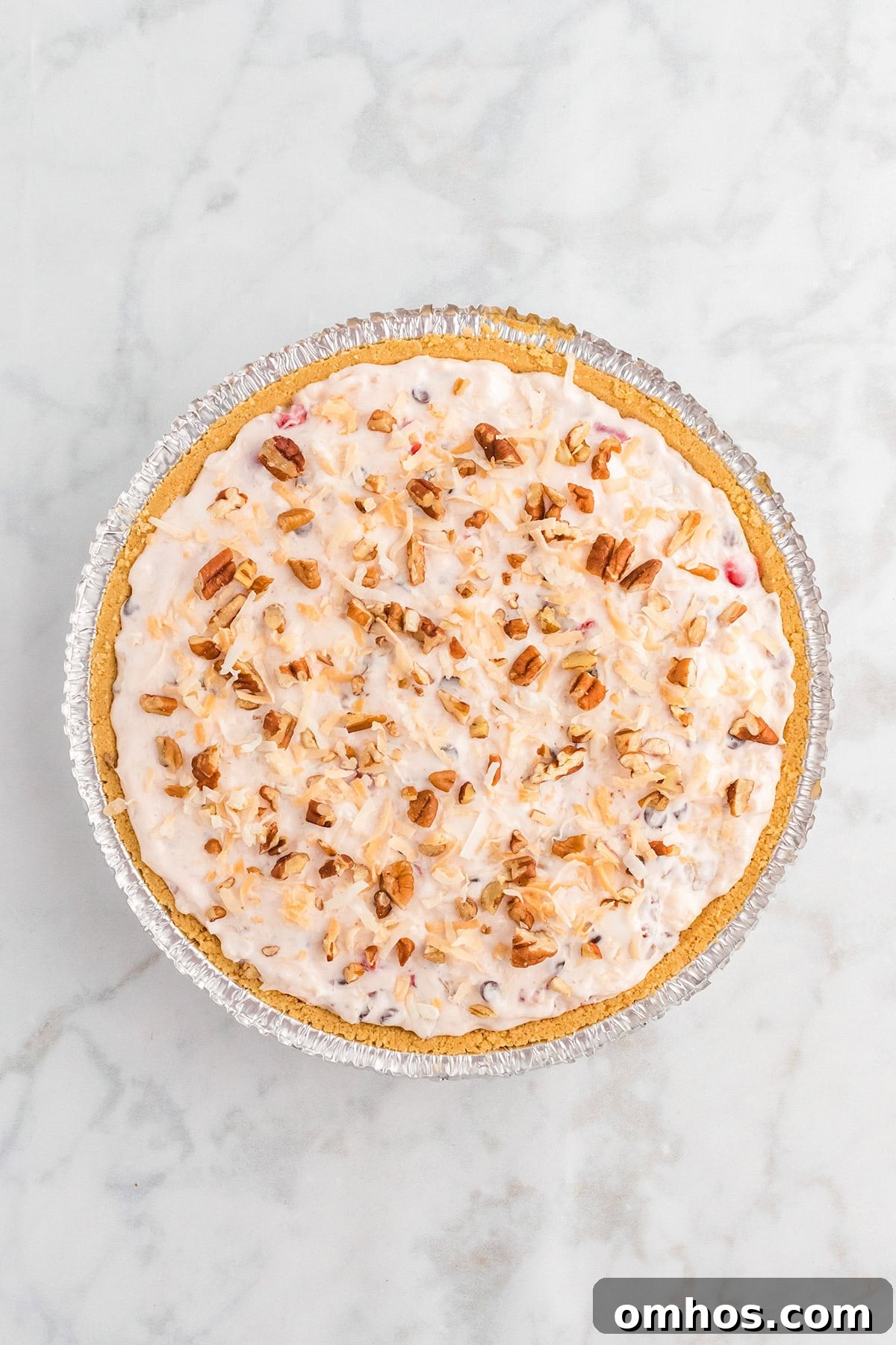 Whole Million Dollar Pie in a graham cracker crust topped with toasted coconut and chopped pecans.