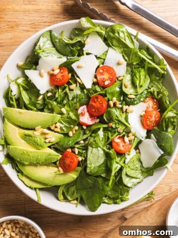 A serving bowl of spinach and arugula salad with a lemon thyme vinaigrette on a butcherblock countertop.
