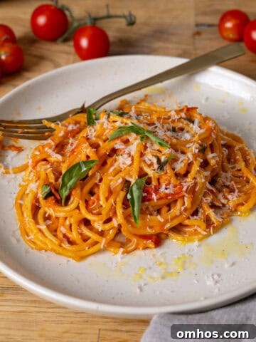 A serving of cherry tomato sauce with spaghetti on a small plate and a skillet with cherry tomatoes in the background.