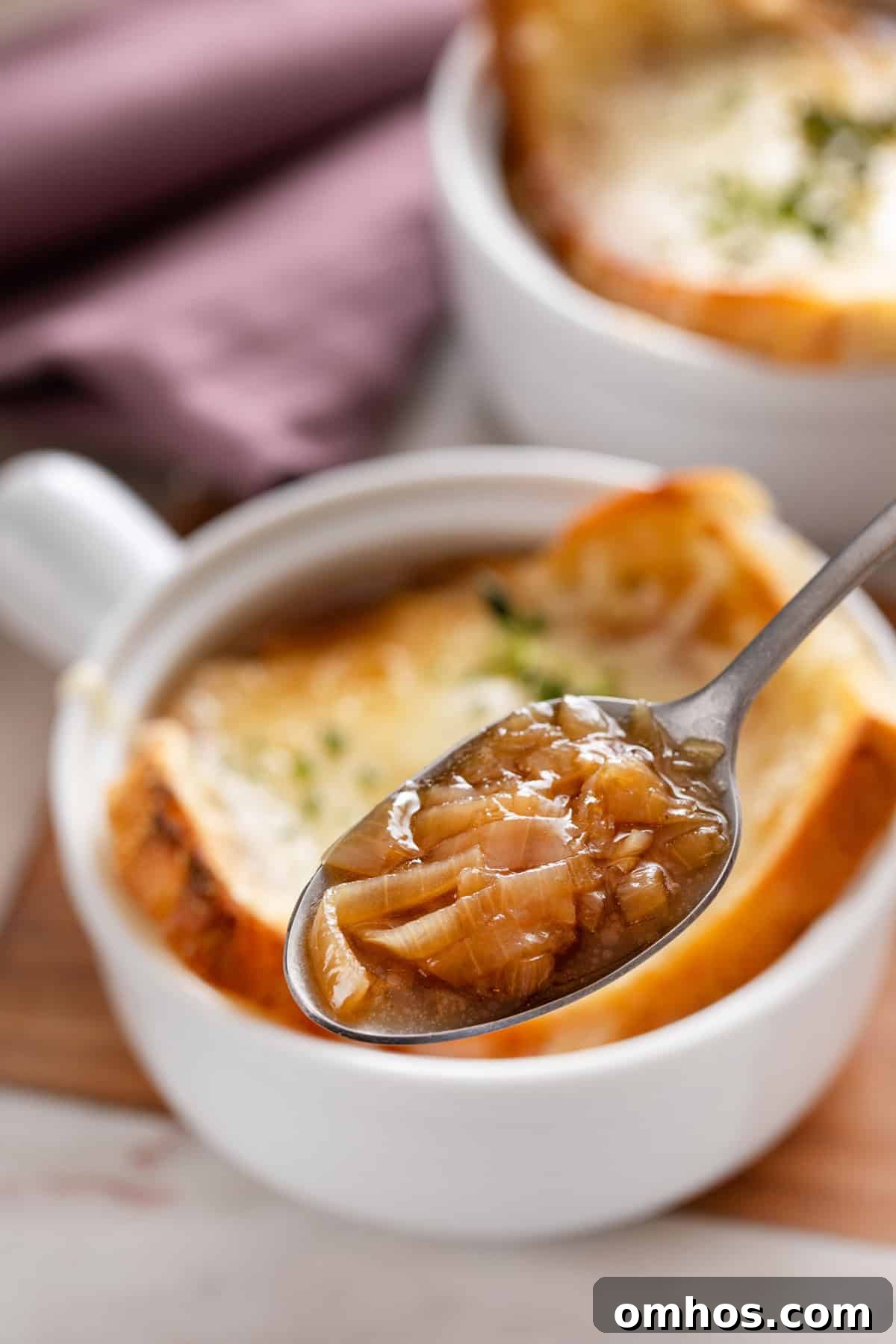 Spoon holding up a bite of french onion soup, with a bowl in the background.