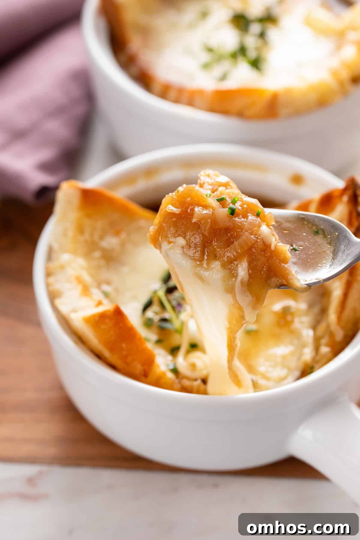 Spoon picking up a bite of french onion soup, showing the cheese pull as the spoon pulls away.