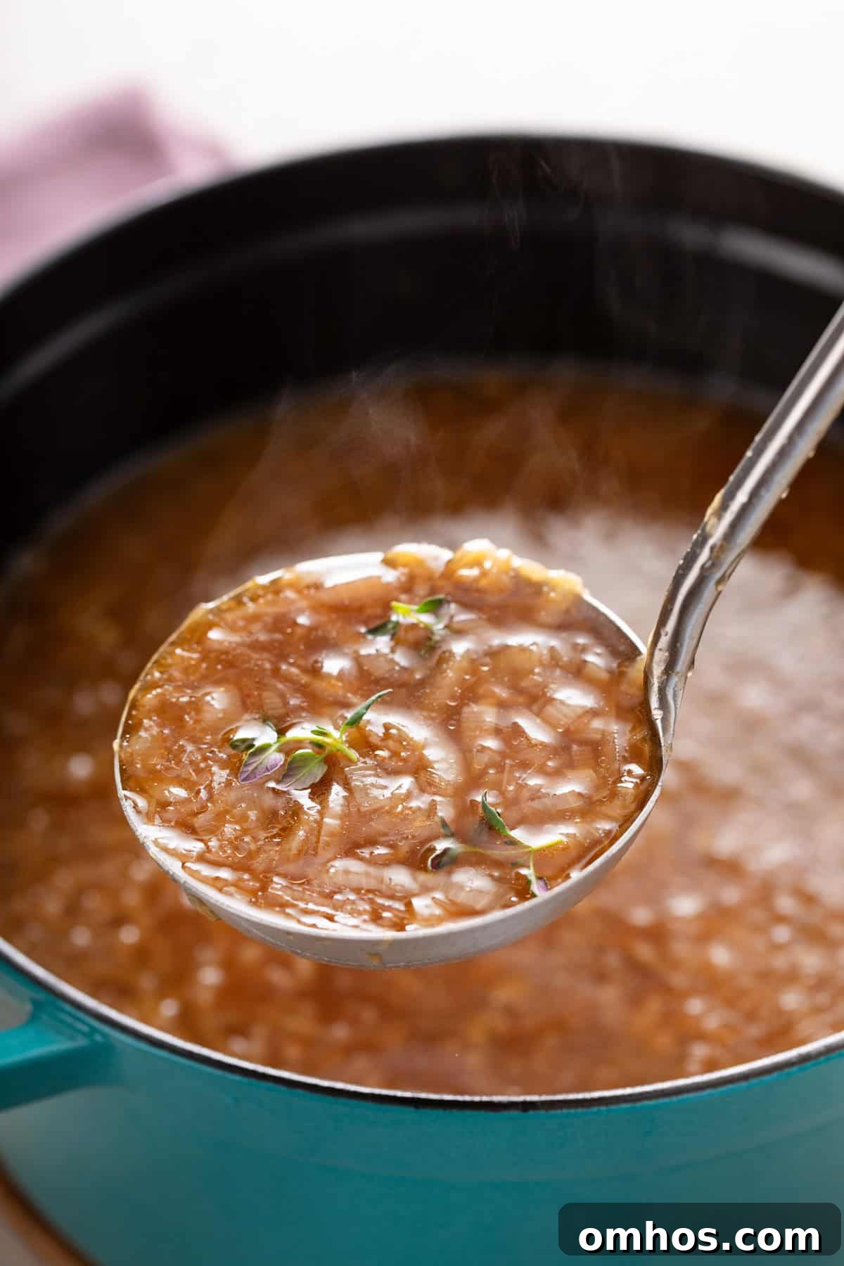 Ladle holding up french onion soup over a pot of the soup.