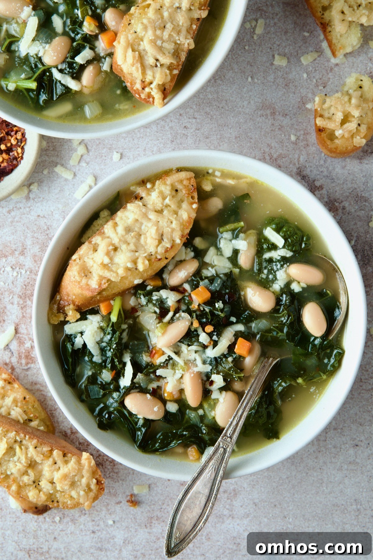 White Bean Kale Soup in white bowl with soup spoon and Parmesan Toast on top.