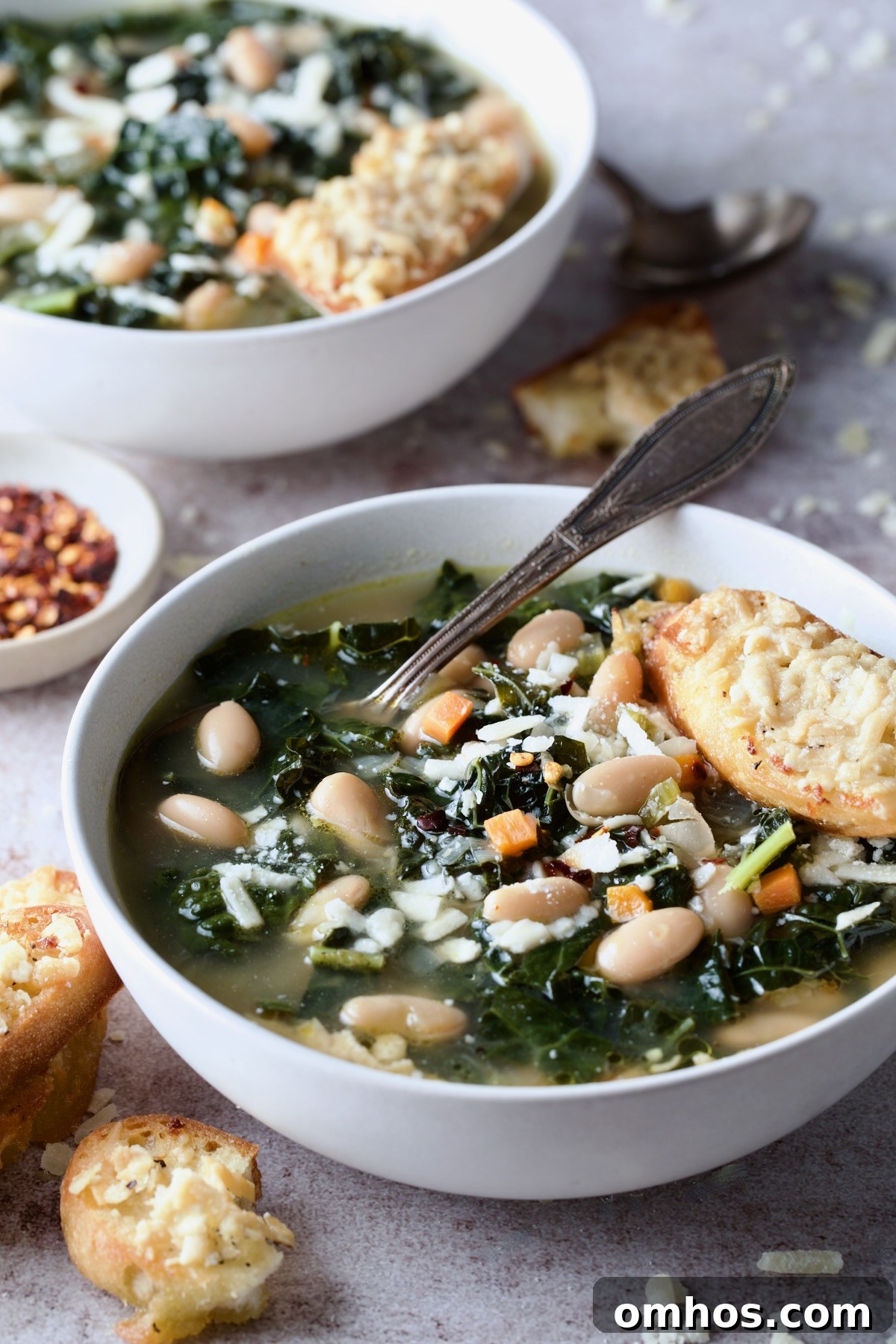 White Bean Kale Soup with Parmesan Toast in white bowl with another bowl in the background.