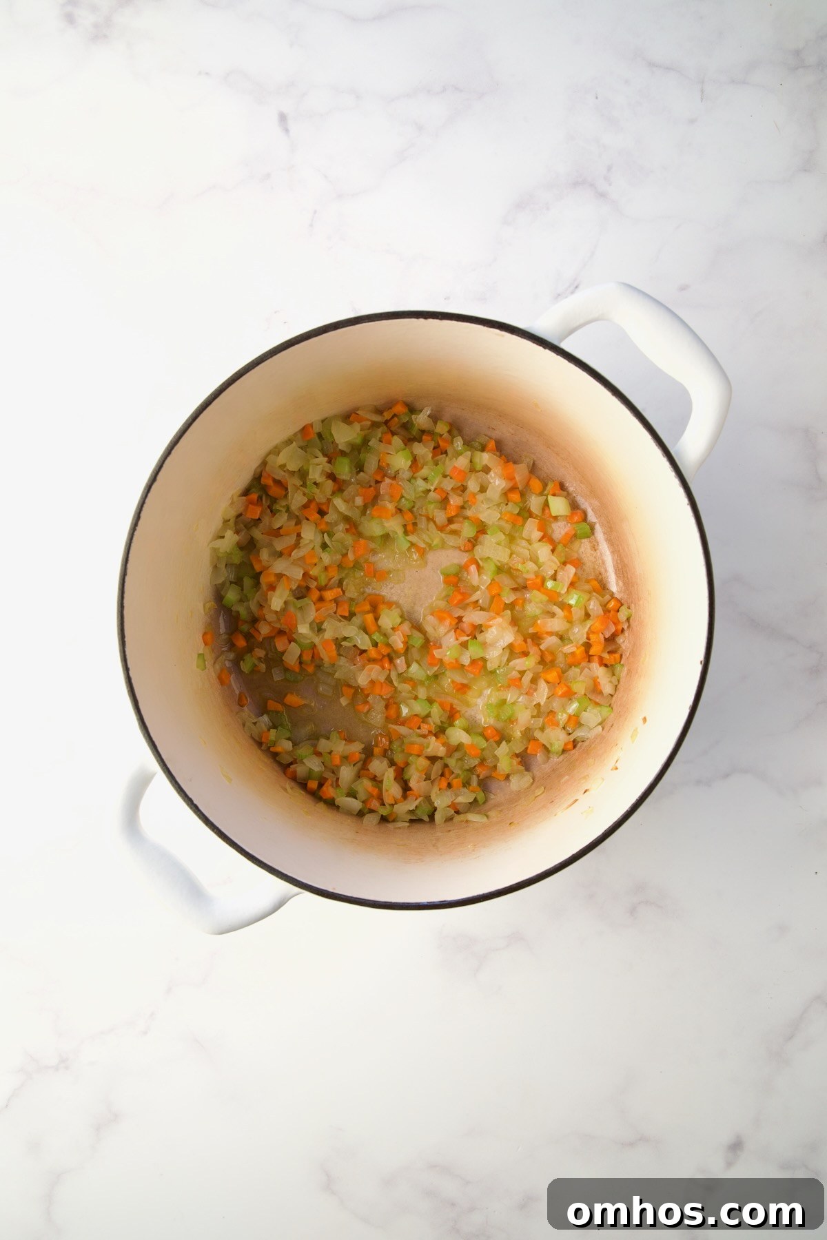 Cooked onions, carrot and celery in white Dutch oven.