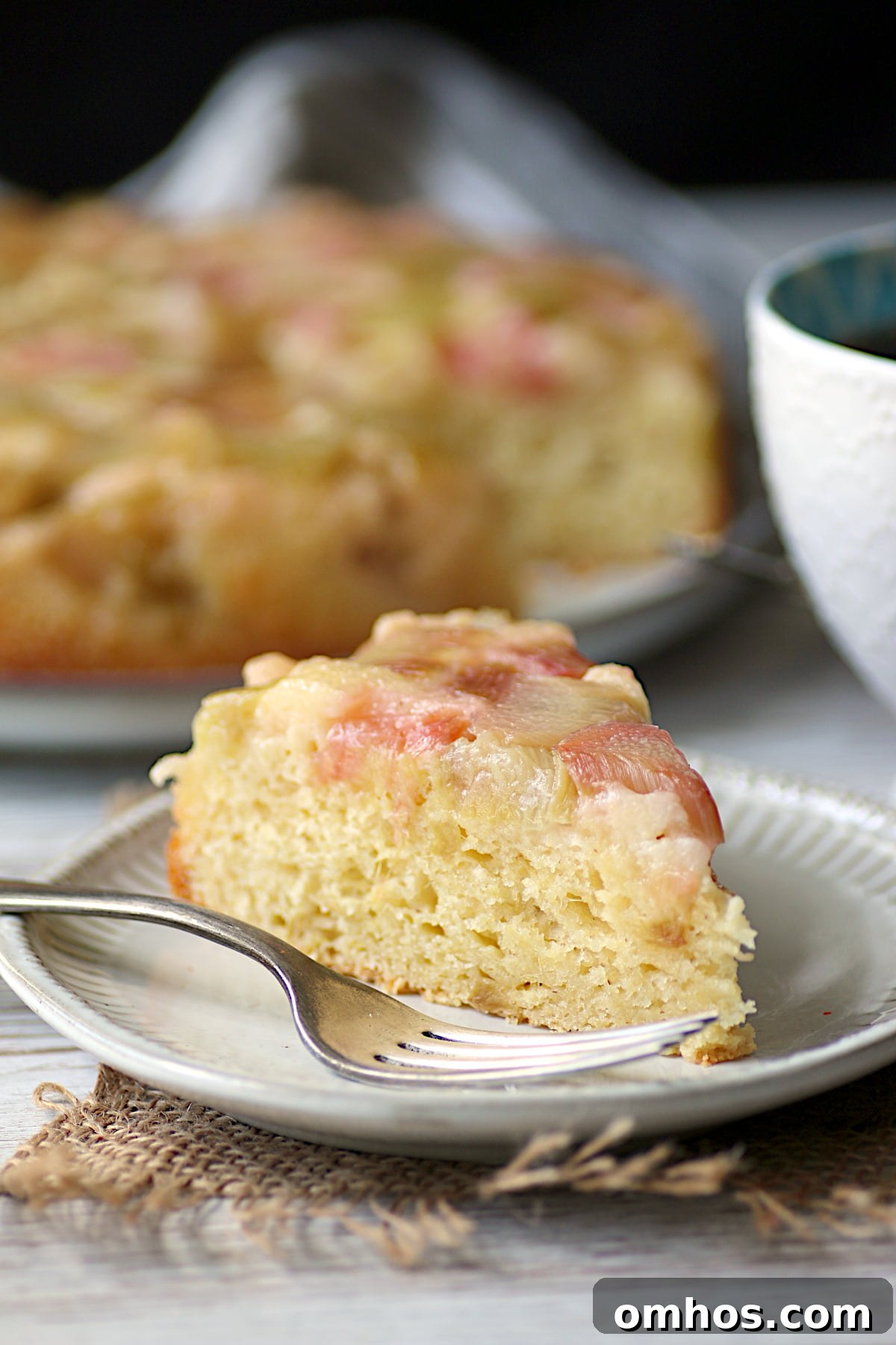 A slice of Cornmeal Rhubarb Upside-Down Cake on a small, white plate.