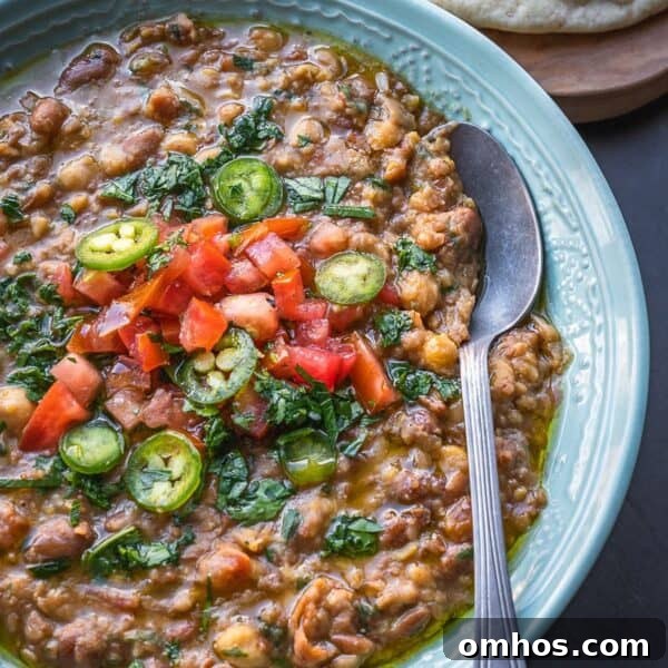 Bowl of mashed fava and chickpeas topped with diced tomatoes and parsley.