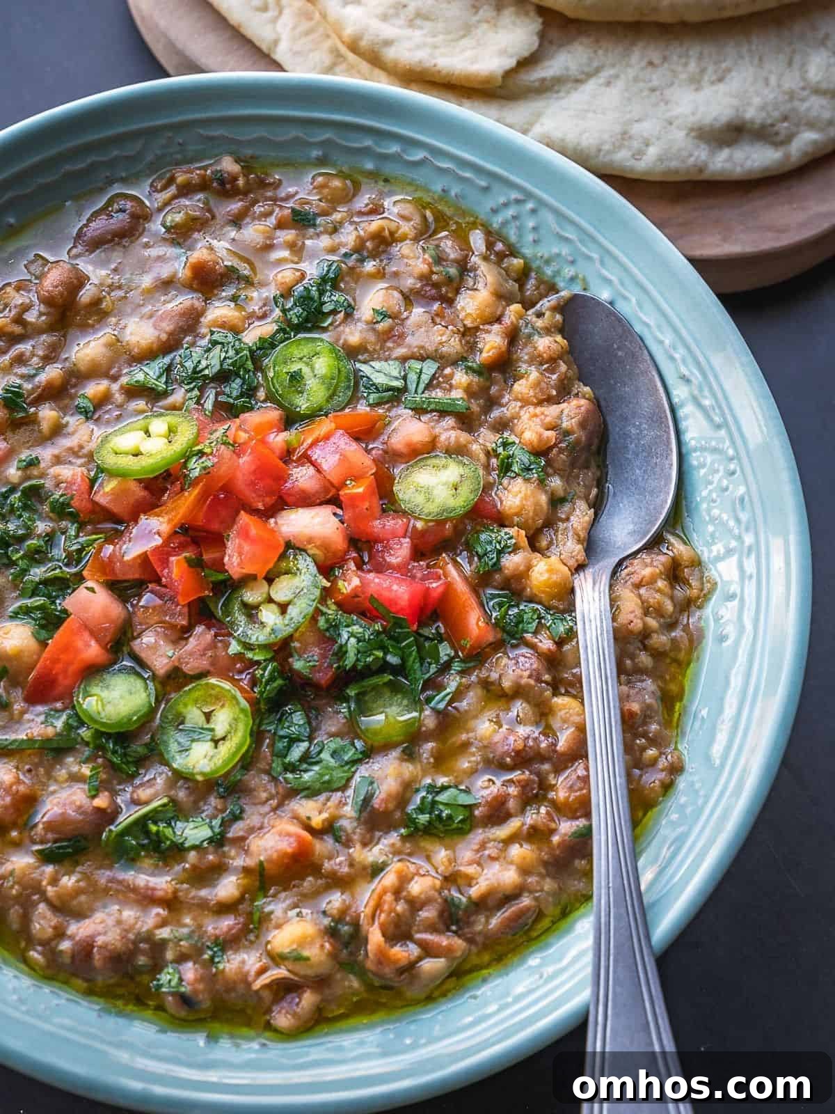 Bowl of mashed fava and chickpeas topped with diced tomatoes and parsley.