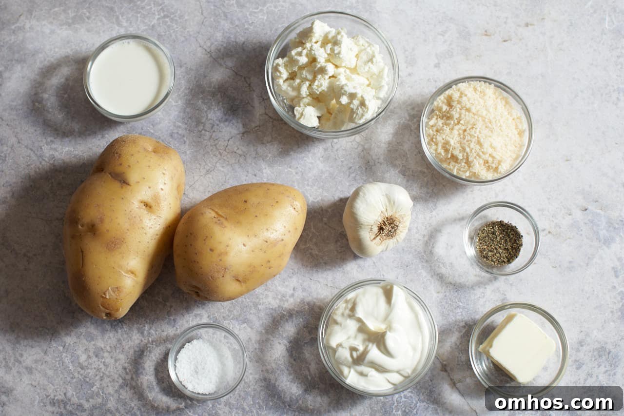 Two Yukon Gold potatoes, a head of garlic, and small glass bowls of cream cheese, sour cream, goat cheese, butter, half and half, salt, and pepper.