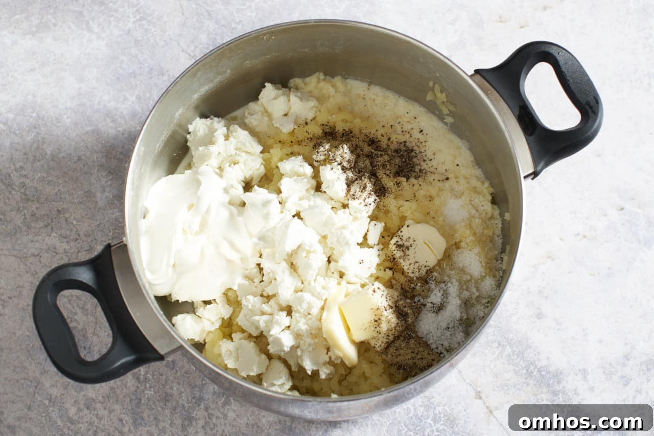 A pot filled with potatoes, butter, cheeses and other ingredients ready to be stirred together.