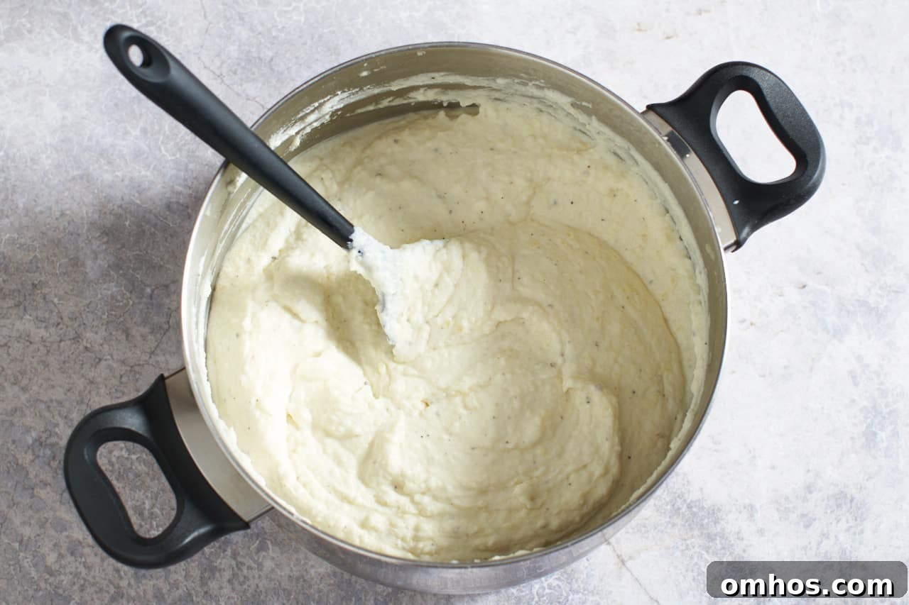 A black spatula in a pot of goat cheese mashed potatoes ready to be transferred to a baking dish.